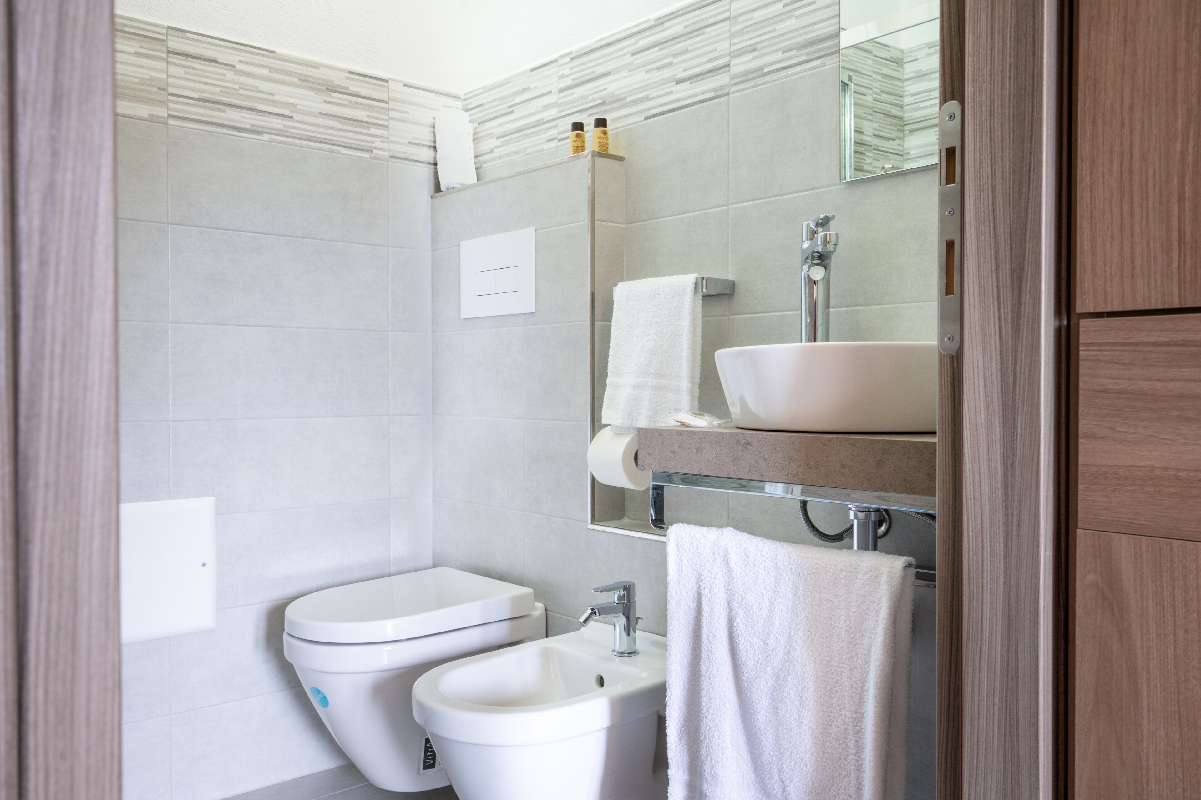 A modern bathroom with a toilet, bidet, sink, and mirror.