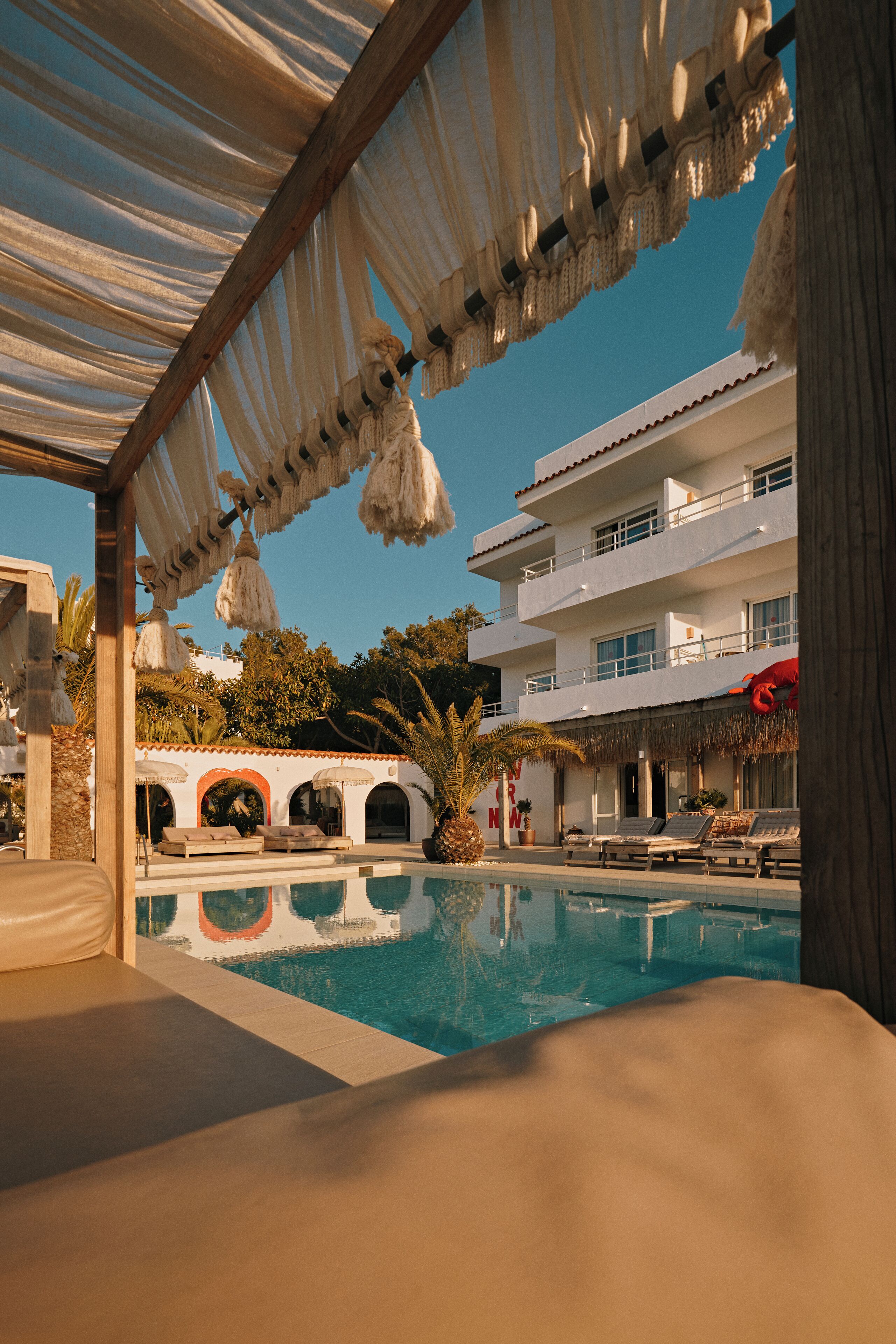 Zona de piscina con sillones de descanso, un edificio con balcones y un cielo azul despejado.