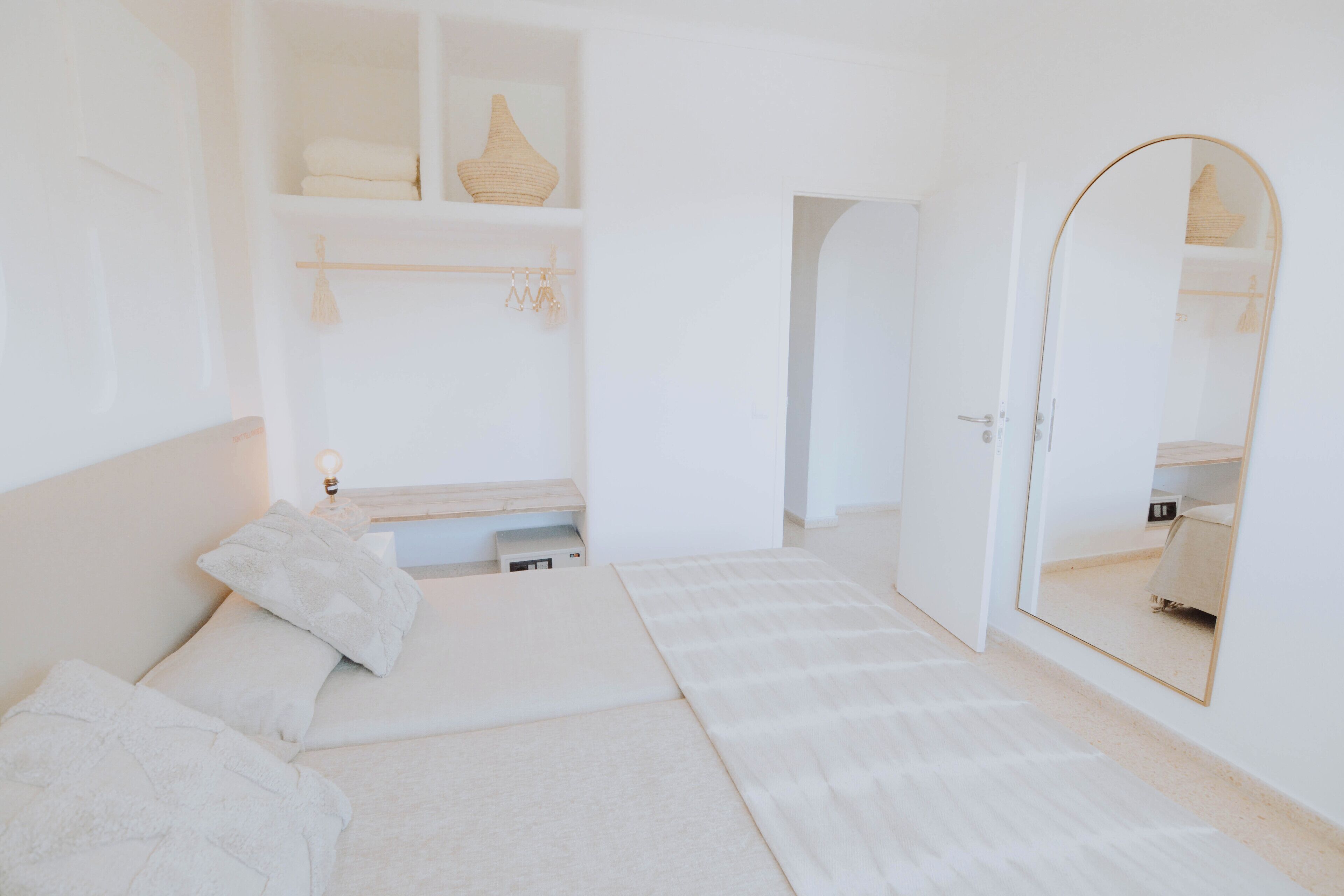 Un dormitorio minimalista con cama, mesita de noche, espejo y armario.