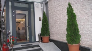 A hotel entrance with a glass door, a metal staircase, and two potted evergreen trees. - VIP Hotel Sarajevo (Sarajevo)