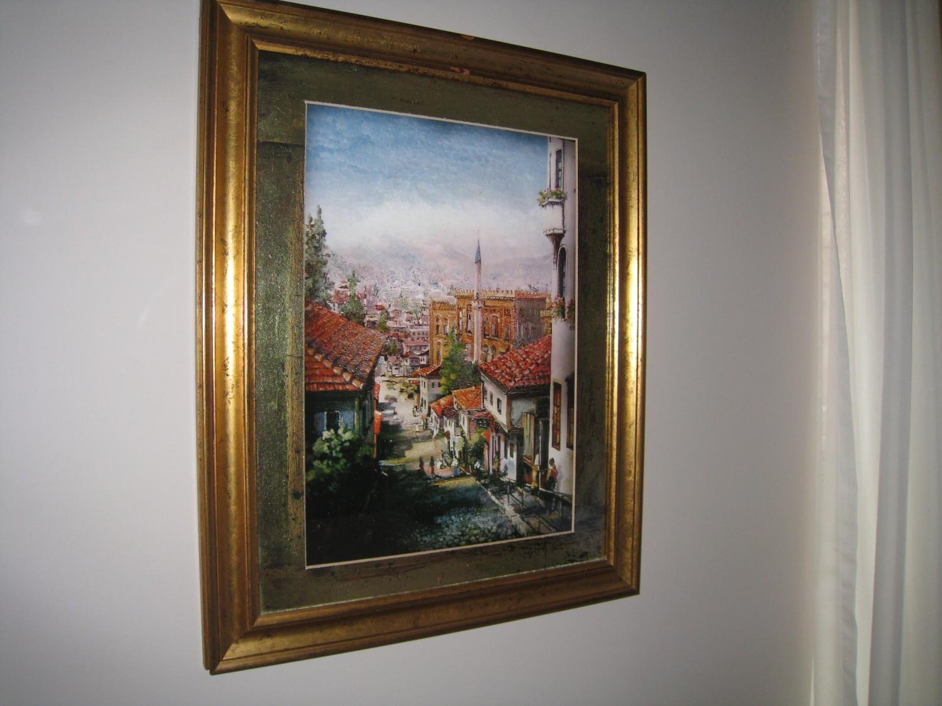 A framed painting of a town with a prominent tower and a river.
