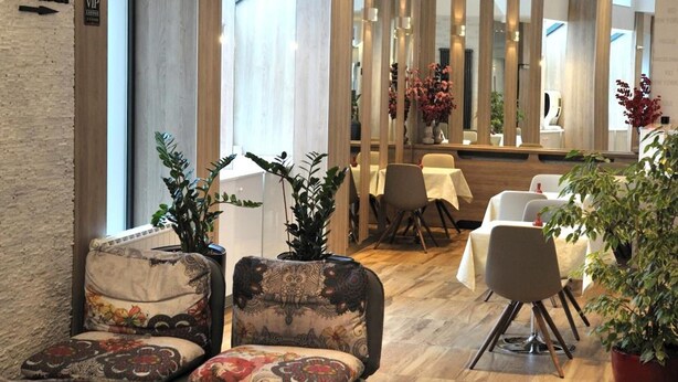 A modern dining area with patterned chairs, a large decorative light fixture, and a view of the restaurant through a glass partition. - VIP Hotel Sarajevo (Sarajevo)