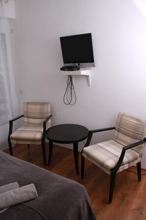 Relax in a clean and functional room with a flat-screen TV, small table, and two armchairs.