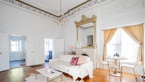 Amplia sala de estar con un sofá blanco, una mesa de centro y una chimenea. Encima de la chimenea hay un espejo grande y un comedor con sillas.