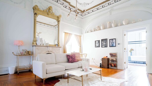 Un salón amplio con sofá blanco, una mesita de centro, un espejo grande y alfombra blanca.