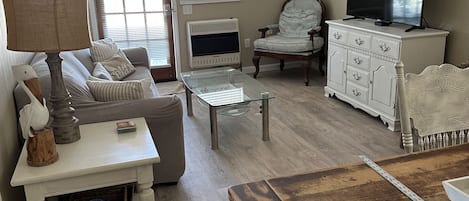 A living room with a sofa, armchair, coffee table, and a TV on a cabinet.