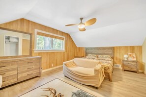 Cozy retreat with a large bed, bedside table, and dresser, offering a view of the outdoors.