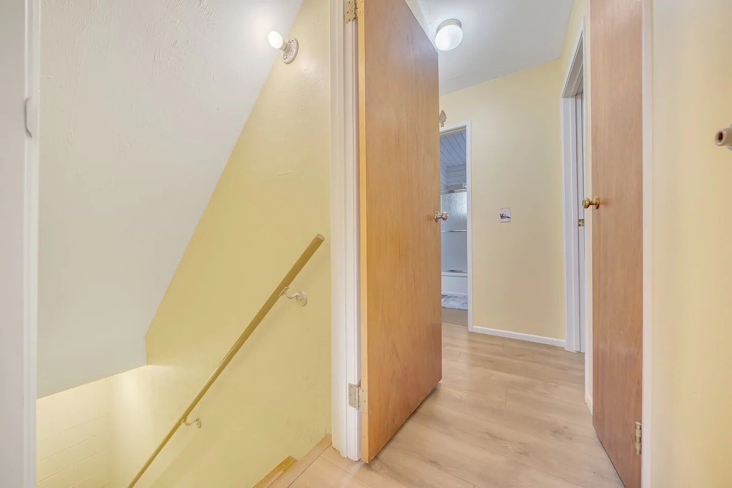 Un couloir avec un escalier en bois, un placard et une porte donnant sur une autre pièce.