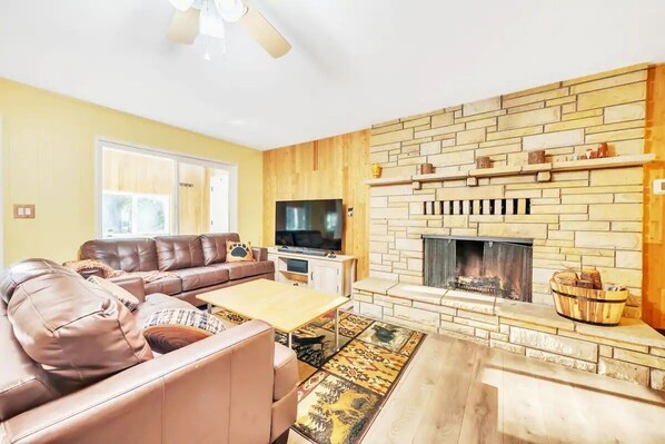 A living room with a stone fireplace, leather sofa, and a flat-screen TV. - Luxe Private Mountainside Getaway in Pioneer! (Pioneer)