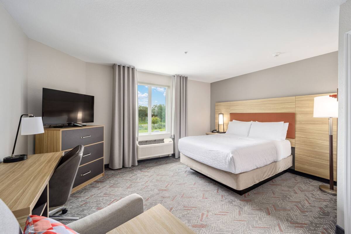 Habitación de hotel con cama, escritorio, silla, televisión y ventana con cortinas.