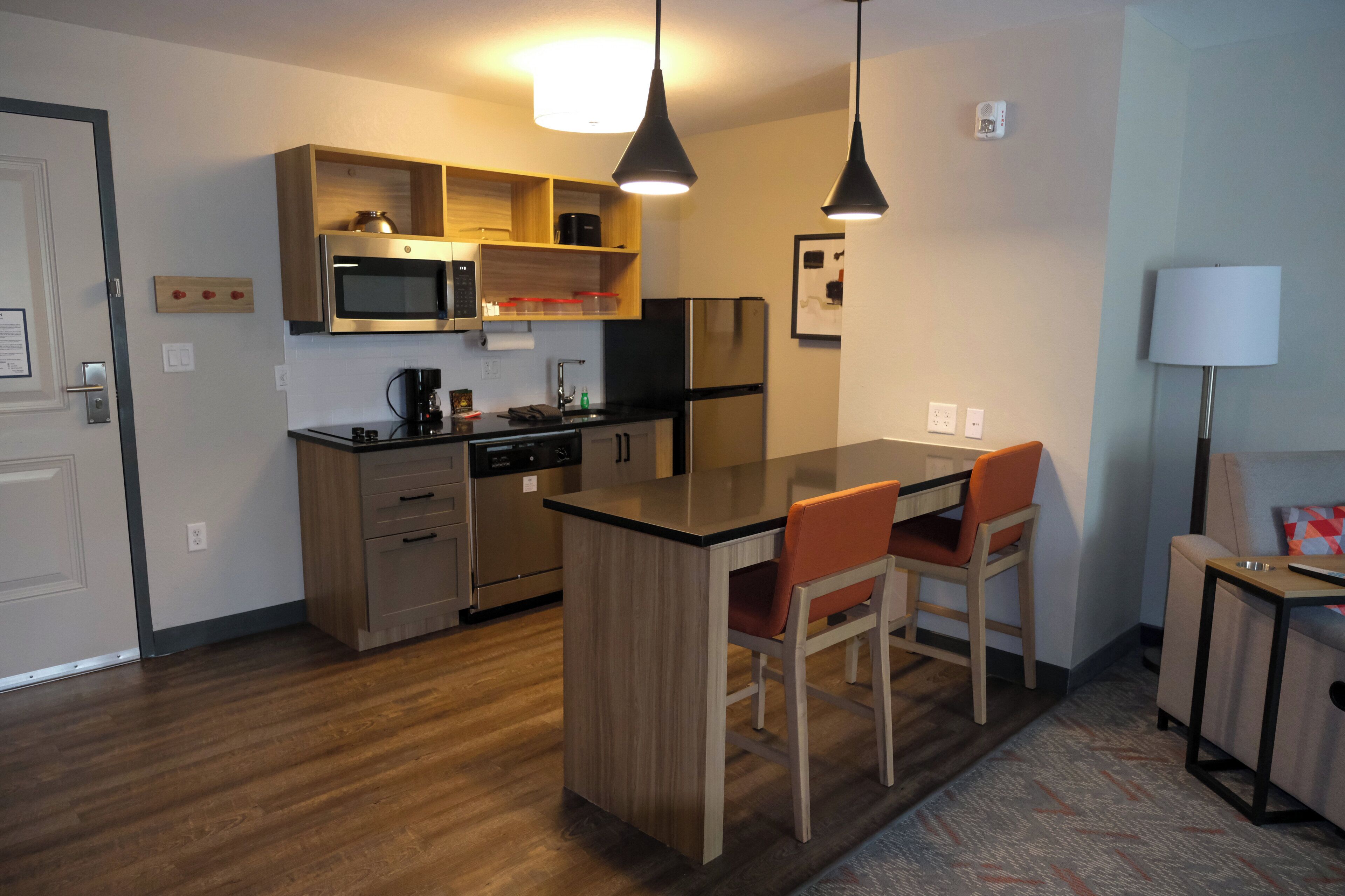 Een moderne keuken met houten kastjes, een ingebouwde magnetron, een koelkast en een eethoek met een tafel en stoelen.