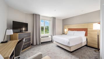 A hotel room with a bed, a desk with a chair, a television, a window with curtains, and a lamp.