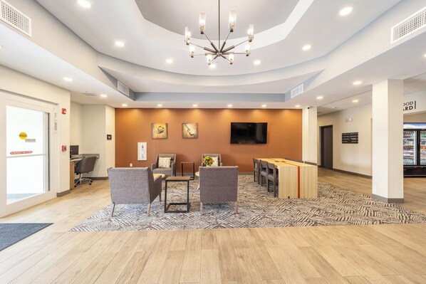 A modern hotel lobby with a chandelier, seating area, and a television on the wall. - Candlewood Suites Ocala I-75 by IHG (Ocala)