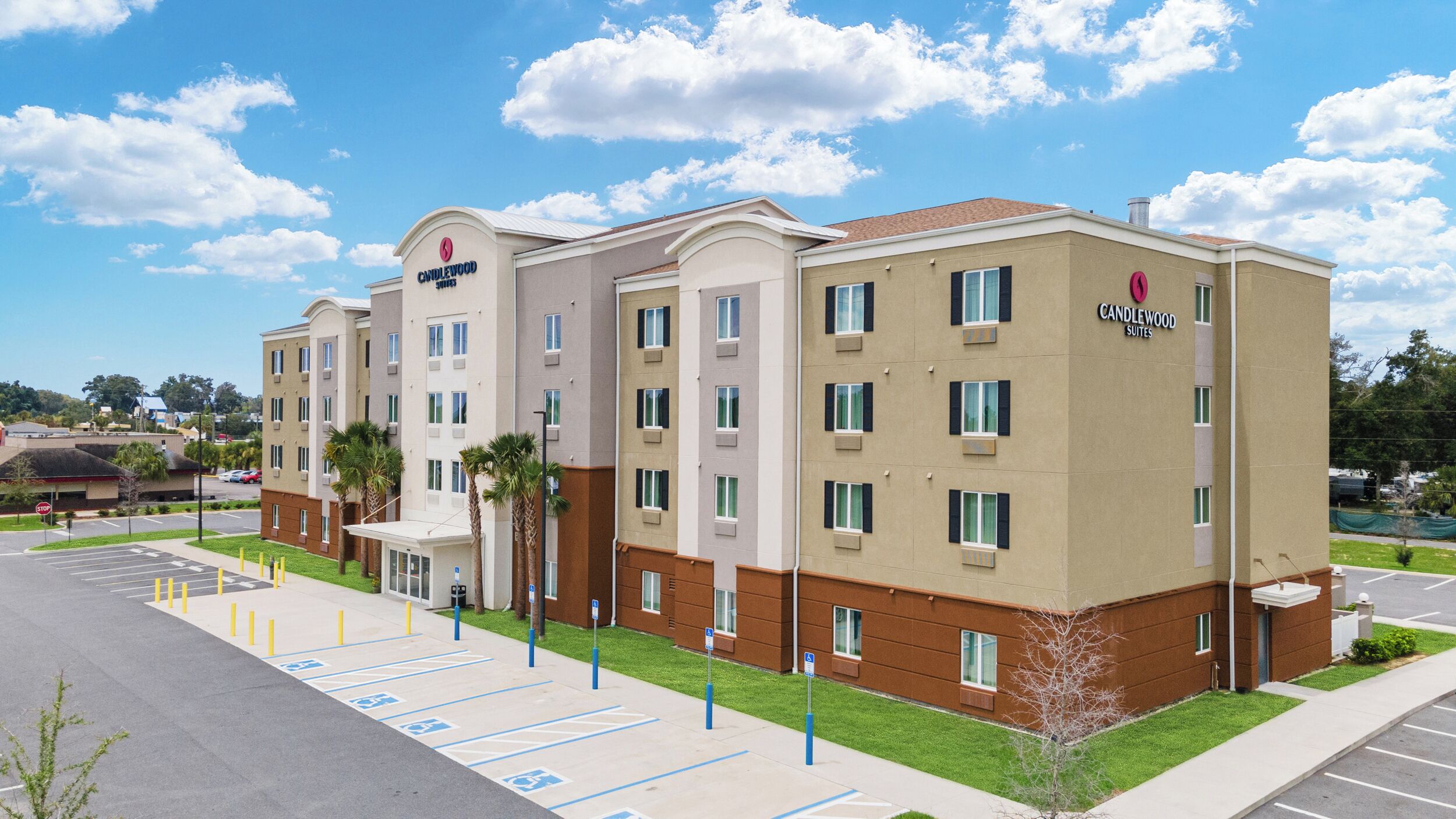 A multi-story hotel with a flat roof, a parking lot with marked handicapped spaces, and a sign indicating 'Candlewood Suites.'