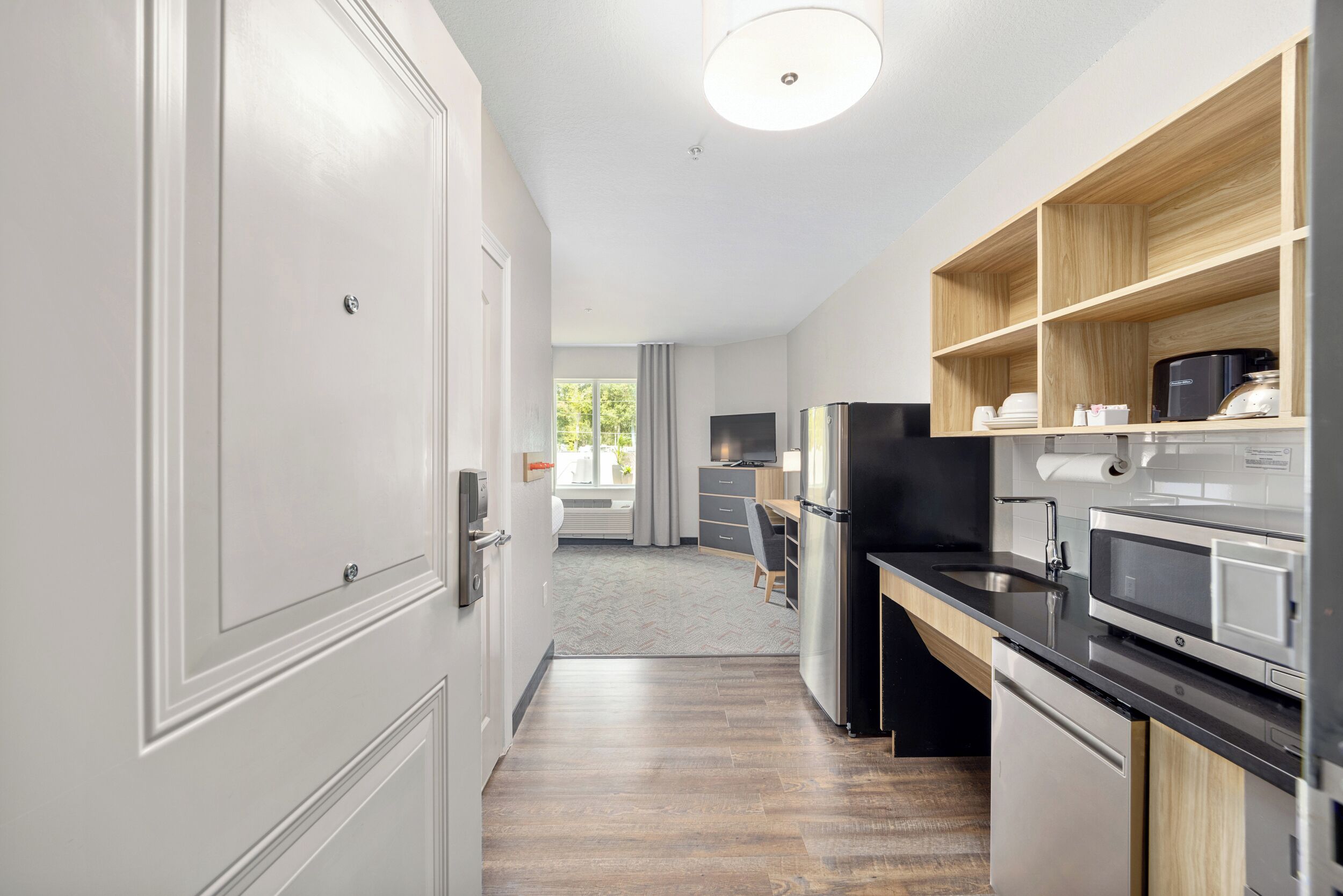 Une cuisine moderne dotée d’appareils électroménagers intégrés, d’une étagère en bois et offrant une vue sur l’espace de vie.