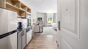Una habitación de hotel moderna con kitchenette, una cama, un escritorio y vistas al exterior.