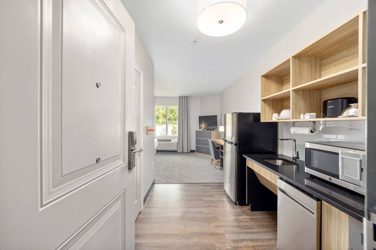 Una cocina moderna con armarios blancos, un refrigerador negro, un microondas y una repisa de madera.