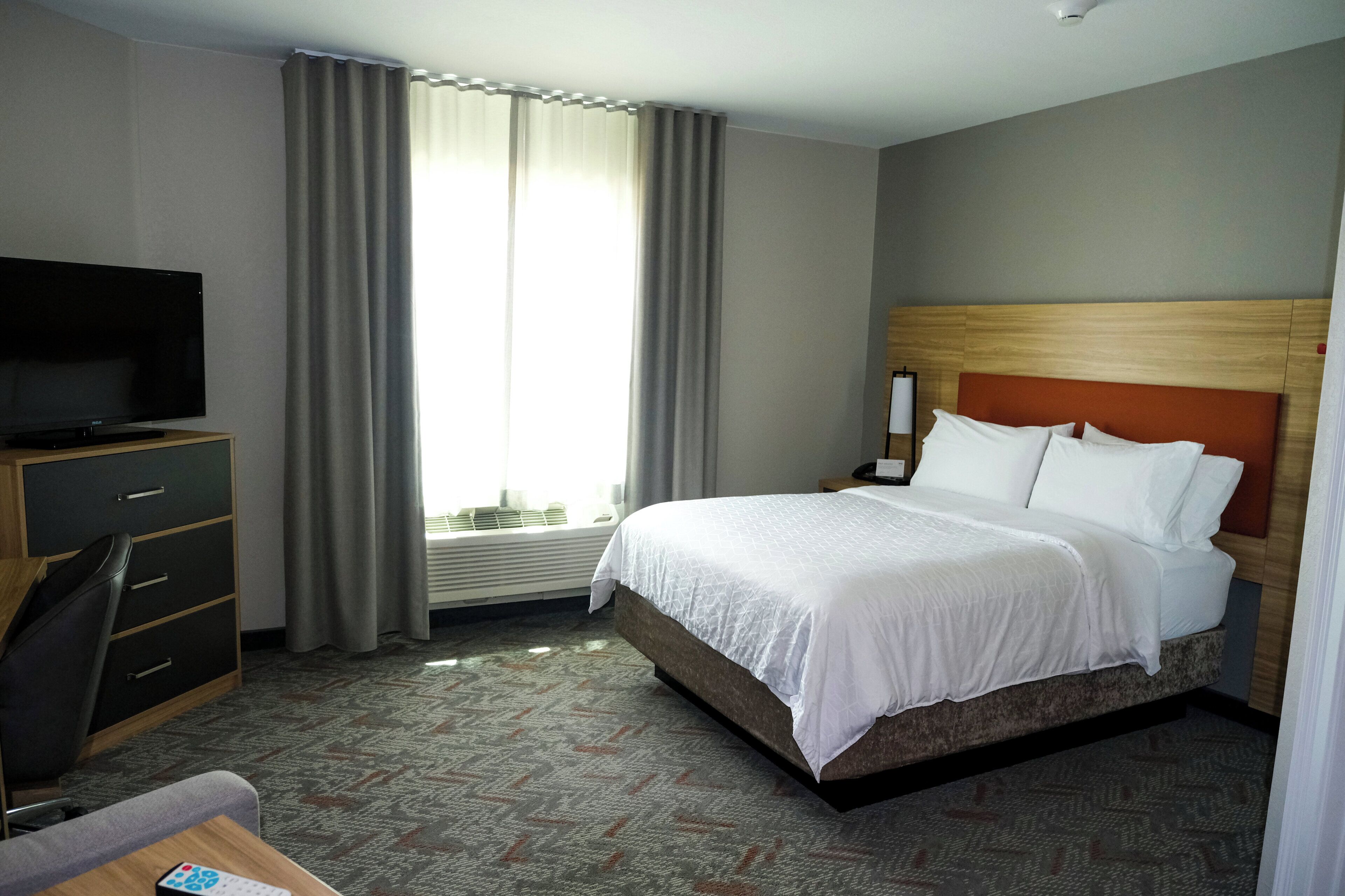 A hotel room with a bed, a desk, a chair, a television, and a window with curtains.