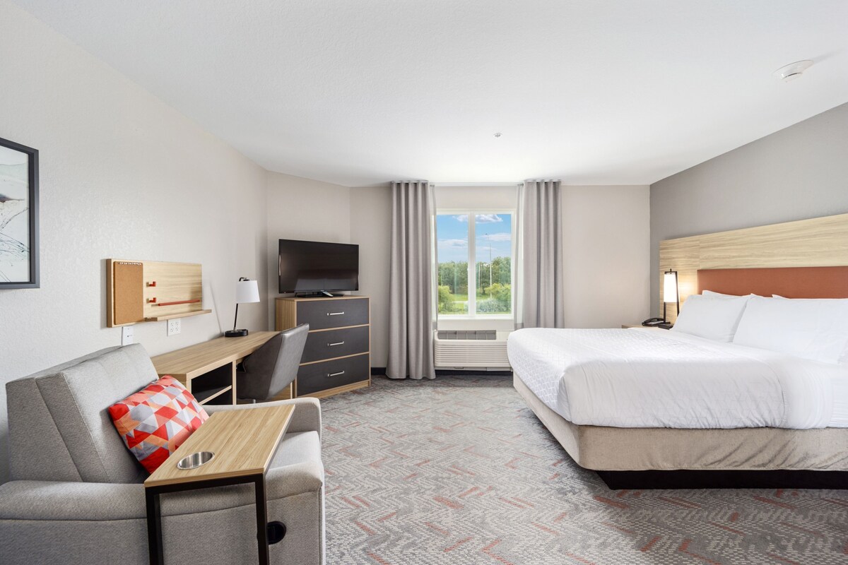 A hotel room with a bed, a desk with a chair, a TV, and a window with curtains.