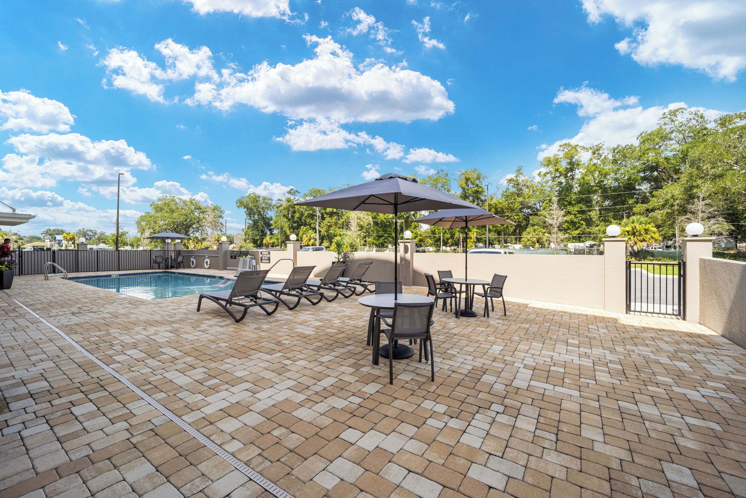 Zona junto a la piscina con sillones, una mesa y una sombrilla.