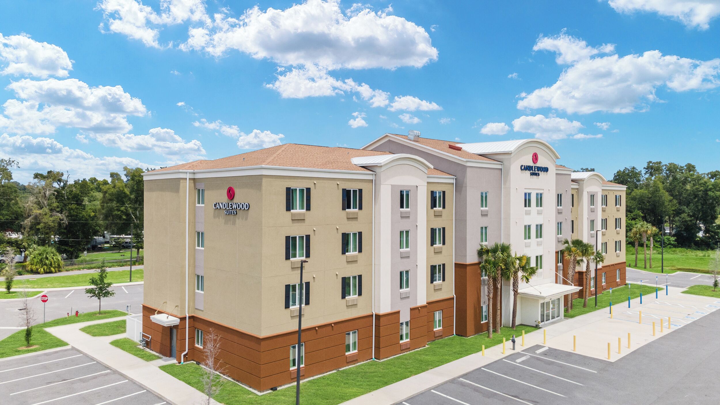 A multi-story hotel with a flat roof, a parking lot, and a landscaped area with palm trees.