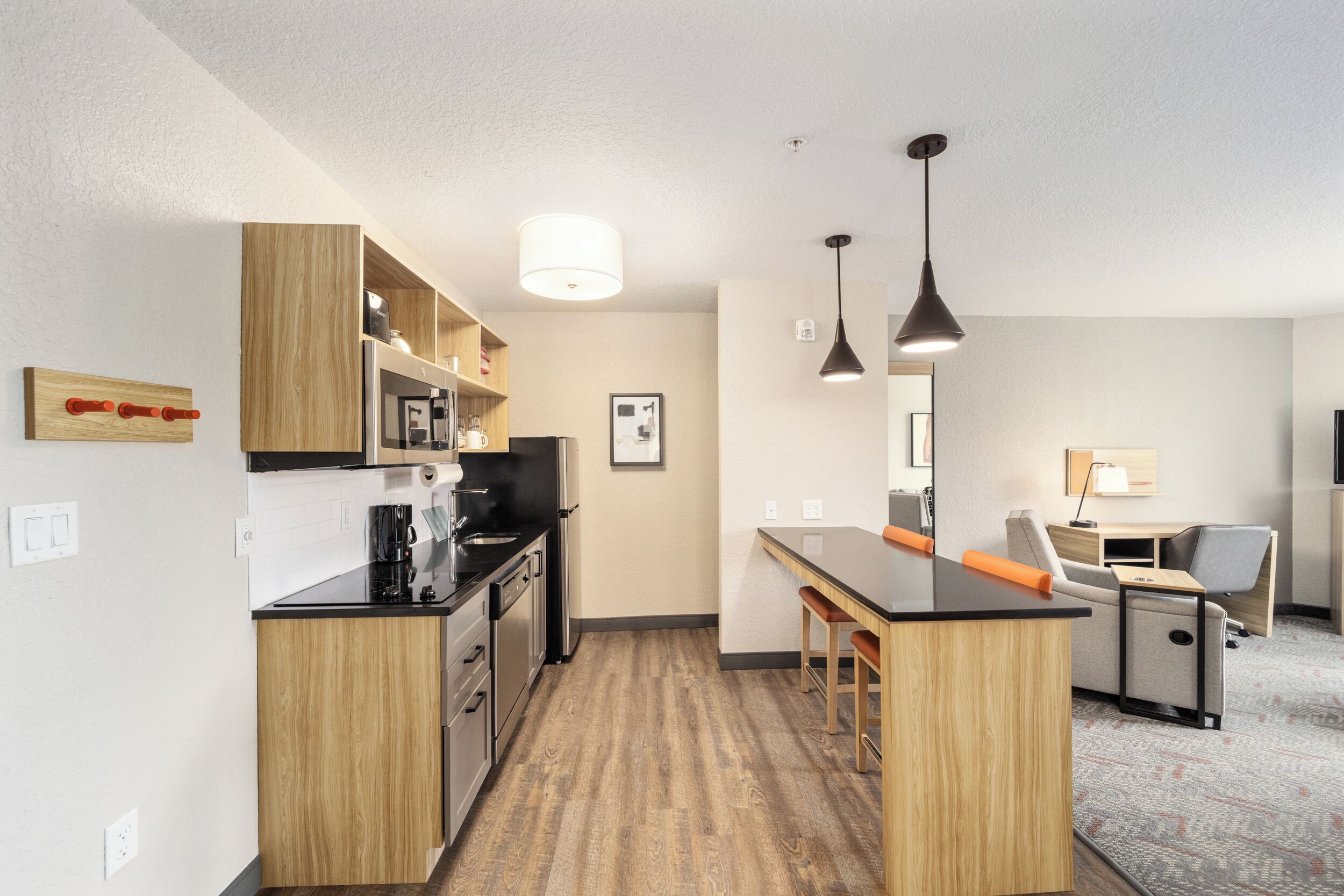 A modern kitchen with wooden cabinets, a central island, bar stools, and pendant lighting.