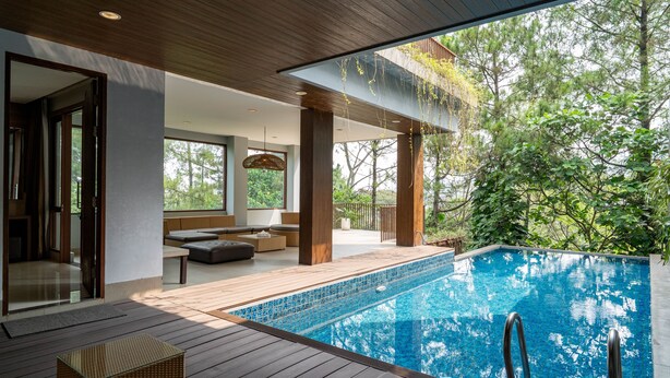 A modern outdoor pool area with wooden decking, a seating area, and a view of trees. - Anindya Hill Villa 7 Br Heated Pool and a Billiard (Bandung)