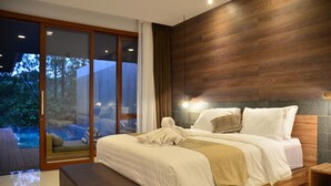 A modern bedroom with a large bed, a wooden headboard, a bench, and a view of a pool and trees. - Anindya Hill Villa 7 Br Heated Pool and a Billiard (Bandung)