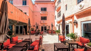 Un patio con mobiliario exterior, plantas en macetas y fachada de edificio con detalles decorativos.