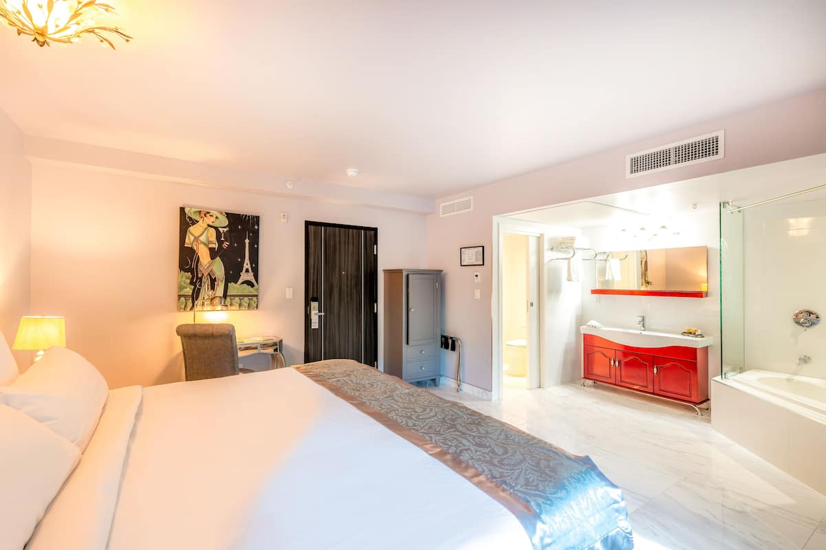 Een hotelkamer met een groot bed, een bureau, een stoel, een garderobe, een badkamer met een rode kast, en een schilderij van een vrouw met de Eiffeltoren.