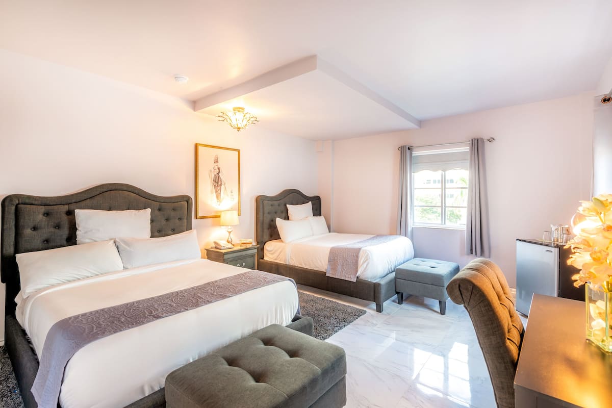 Hotelkamer met twee bedden, een bureau, een stoel, een tafeltje, een spiegel, een raam met gordijnen en een kroonluchter.