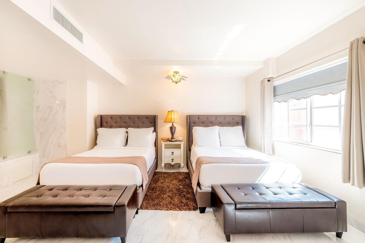 Een hotelkamer met twee bedden, een nachtkastje, een lamp, een raam met gordijnen en een marmeren wand.