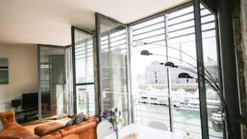 Un salon moderne avec une grande fenêtre, un canapé, une table ornée d’un vase et un téléviseur.