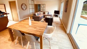 A modern living space with a wooden dining table, white chairs, a sofa, and a TV.