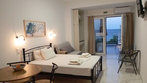 A hotel room with a bed, bedside table, and chairs. There is a balcony with a view of the sea. - Creta Sun Apartments (Ierapetra)