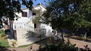 Una casa de dos pisos con escaleras de piedra, un balcón y un jardín con plantas en macetas.