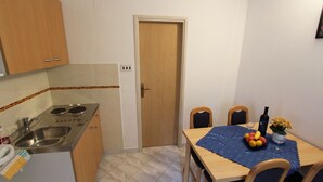 Une cuisine compacte équipée d’une cuisinière, d’un évier et de meubles de rangement en bois. On y trouve une table à manger avec des chaises et un set de table bleu.