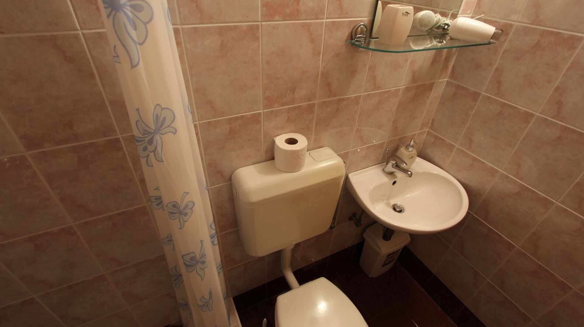 Un baño con inodoro, lavabo y repisa de vidrio sobre el lavabo.
