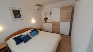 Une chambre à coucher comprenant un lit, une commode, une table de chevet et un climatiseur fixé au mur.
