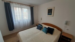 Une chambre à coucher avec un lit, une table de chevet, une fenêtre avec des rideaux et un tableau encadré au mur.