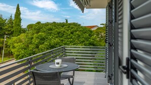 A balcony with a table and chairs, a potted plant, and a view of greenery and a building in the background. - Modern apartment Pivas 2 , ideal for families with children, near the beach and the center (Malinska)