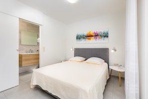 Quarto com cama, mesa de cabeceira, espelho e uma pintura abstrata colorida na parede.