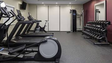 Un gimnasio con cintas de correr, elípticas y un estante con mancuernas.