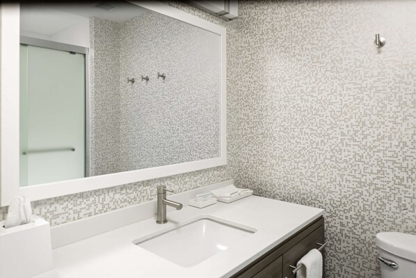 Un baño con lavamanos blanco, un espejo y un inodoro. Las paredes tienen un diseño de azulejos estampados.