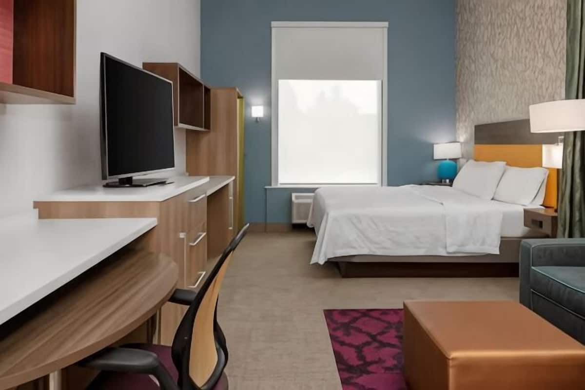 Ein Hotelzimmer mit Bett, Schreibtisch, Stuhl, Fernseher und Fenster.