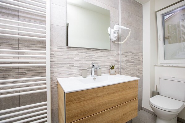 A modern bathroom with a white vanity, a mirror, a hairdryer, and a toilet.