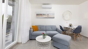 A modern living room with a grey sofa, a small round table, and a dining area with a white table and chairs.