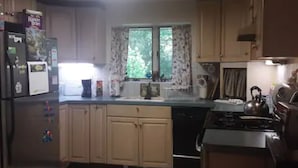 Una cocina con armarios de madera, un refrigerador, una estufa y una ventana con cortinas.