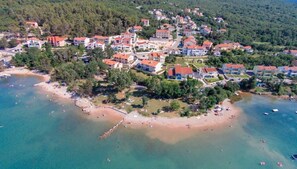 An aerial view of a coastal town with residential buildings, a beach, and clear blue waters.