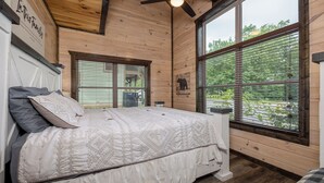Un dormitorio de madera con cama, ventanas amplias y ventilador de techo.